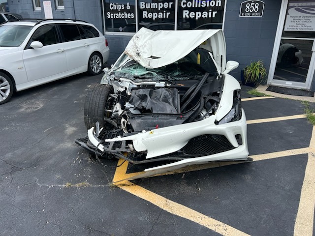 Severely damaged white vehicle with extensive front-end collision damage parked outside a Columbus auto body shop specializing in bumper repair, collision repair, and refinishing.