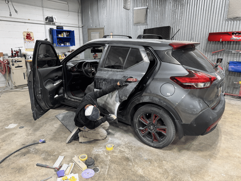Auto body technician repairing and sanding the rear door panel of a gray SUV inside Eurotech’s workshop during a professional paint and body restoration process.