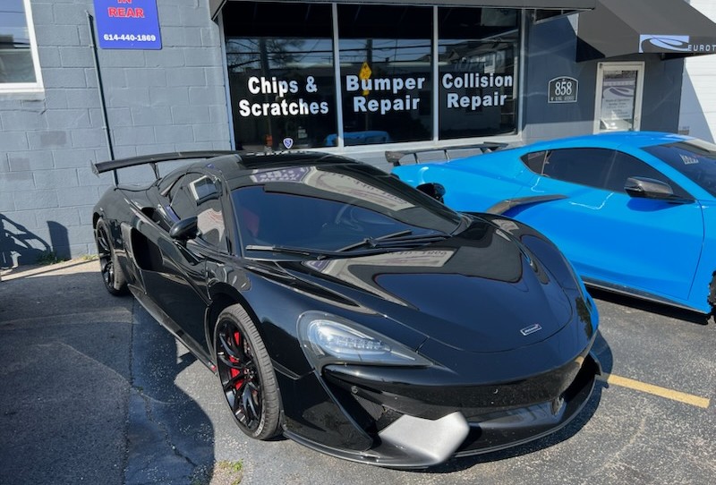 Black McLaren sports car parked outside Eurotech Auto Body Shop in Columbus, OH, with signs for chips, scratches, bumper repair, and collision repair visible in the background.